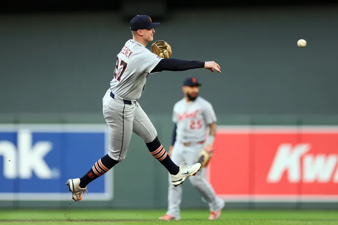 Detroit Tigers infielder leaping off his right foot to make an off-balance throw across the infield at Target Field with a teammate visible in the background