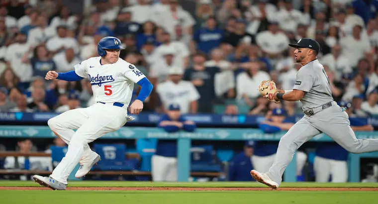 A Los Angeles Dodgers baserunner wearing No. 5 races toward first base while a New York Yankees infielder moves in to make the tag during the Yankees vs Dodgers game at Dodger Stadium on June 1, 2025