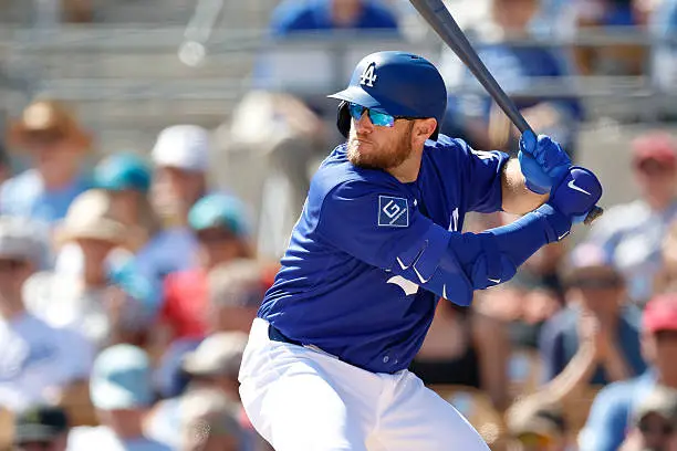 Max Muncy of the Los Angeles Dodgers locked in his batting stance during spring training, wearing full blue Dodgers uniform with sunglasses, ready to swing at an incoming pitch