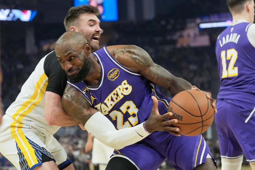 LeBron James #23 of the Los Angeles Lakers drives through contact against a Golden State Warriors defender as Jake LaRavia #12 looks on at Chase Center on April 9, 2026