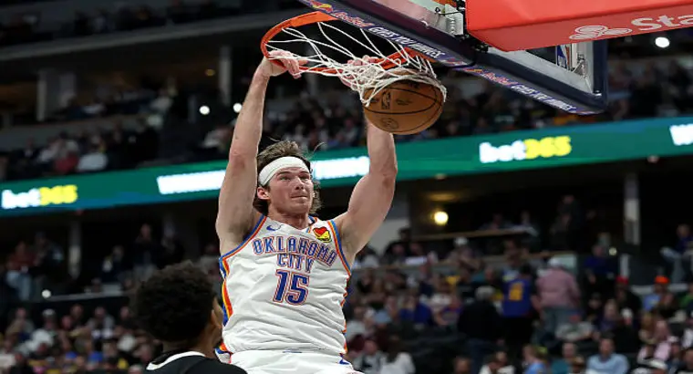 Oklahoma City Thunder's #15 executing a powerful two-handed dunk over a Denver Nuggets defender during an NBA game at Ball Arena in Denver.