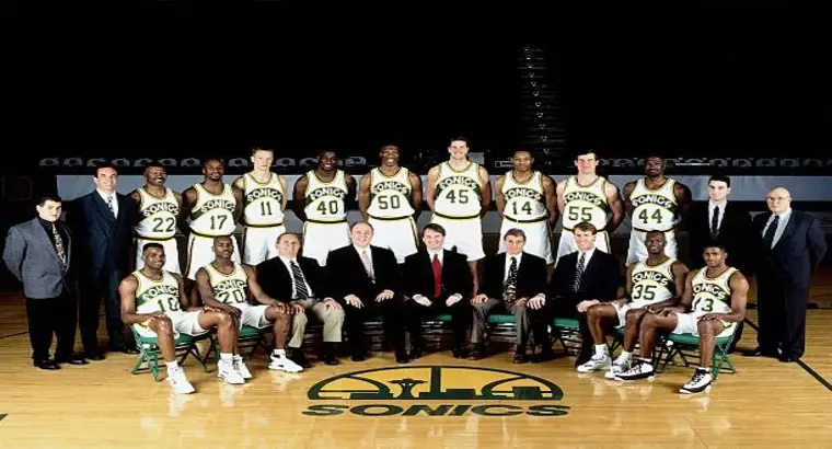 The Seattle SuperSonics full team and coaching staff posing for an official NBA team photograph on their home court in the early 1990s, wearing their classic green and gold uniforms.
